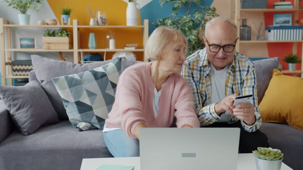 Äldre par som använder bärbar dator och betalkort i soffan.