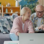 Äldre par som använder bärbar dator och betalkort i soffan.
