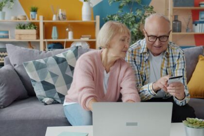 Äldre par som använder bärbar dator och betalkort i soffan.