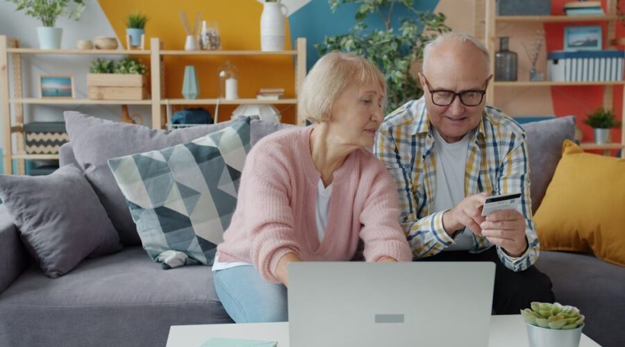 Äldre par som använder bärbar dator och betalkort i soffan.