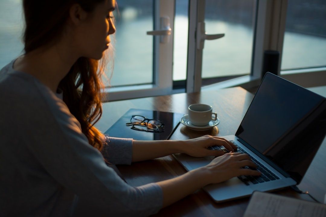 Person arbetar vid laptop med kaffe och glasögon vid ett fönster