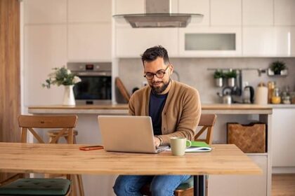 Man arbetar vid laptop i ett kök, med kaffekopp och anteckningsbok